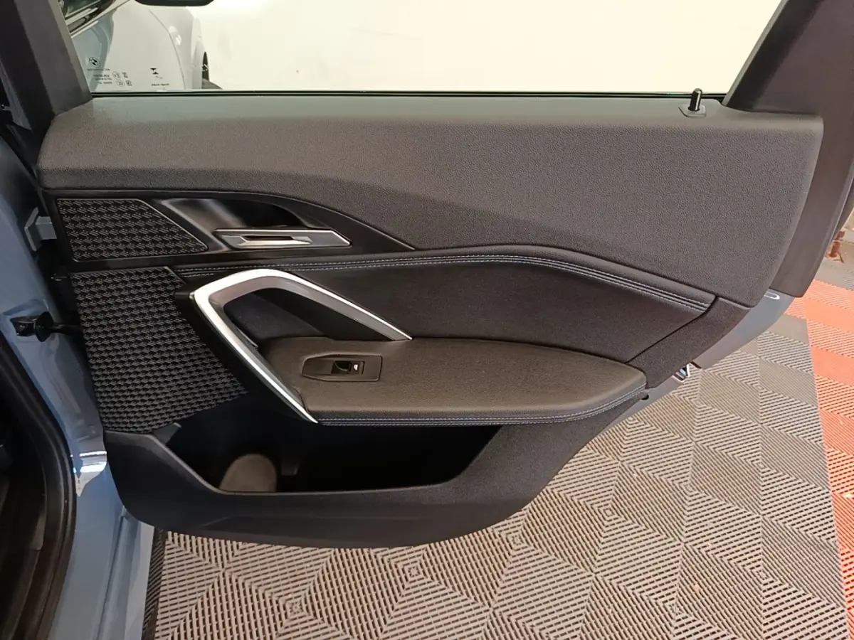 Vue intérieure côté gauche de la porte arrière grise du BMW X1 xDrive25e M Sport 2023 avec garniture noire et surpiqûres bleues.