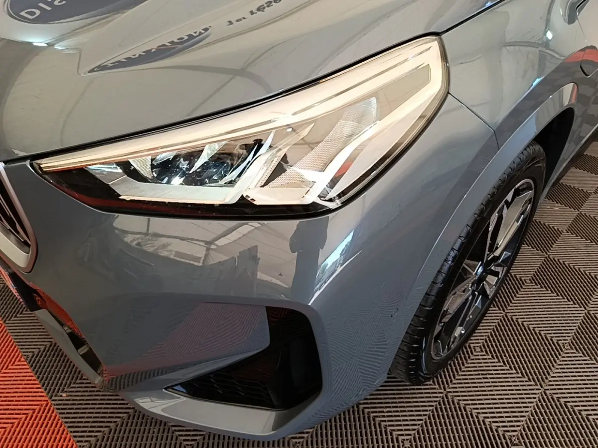 Gros plan sur l'avant droit du BMW X1 xDrive25e M Sport gris foncé, mettant en valeur le phare LED et la jante alliage.