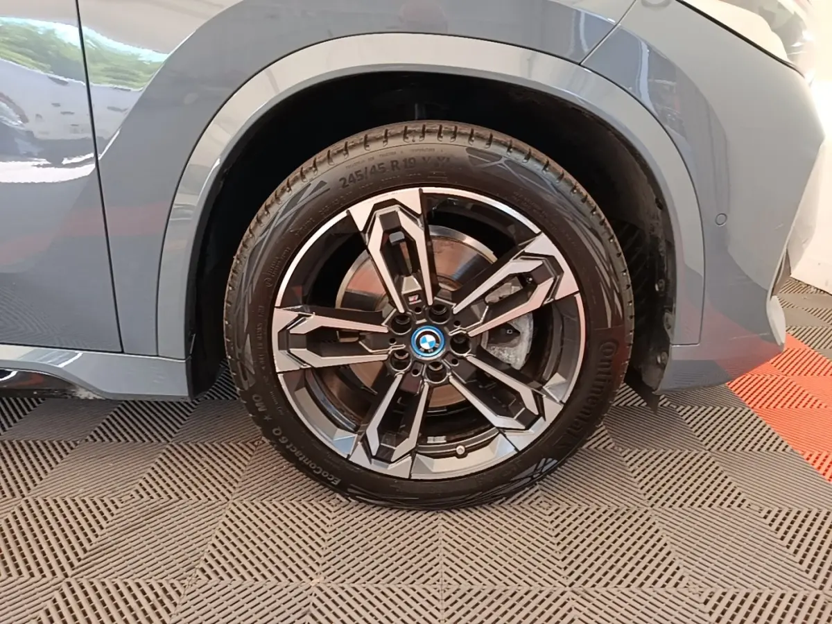 Gros plan sur la roue avant gauche d’un BMW X1 gris foncé avec jante alliage au design géométrique.