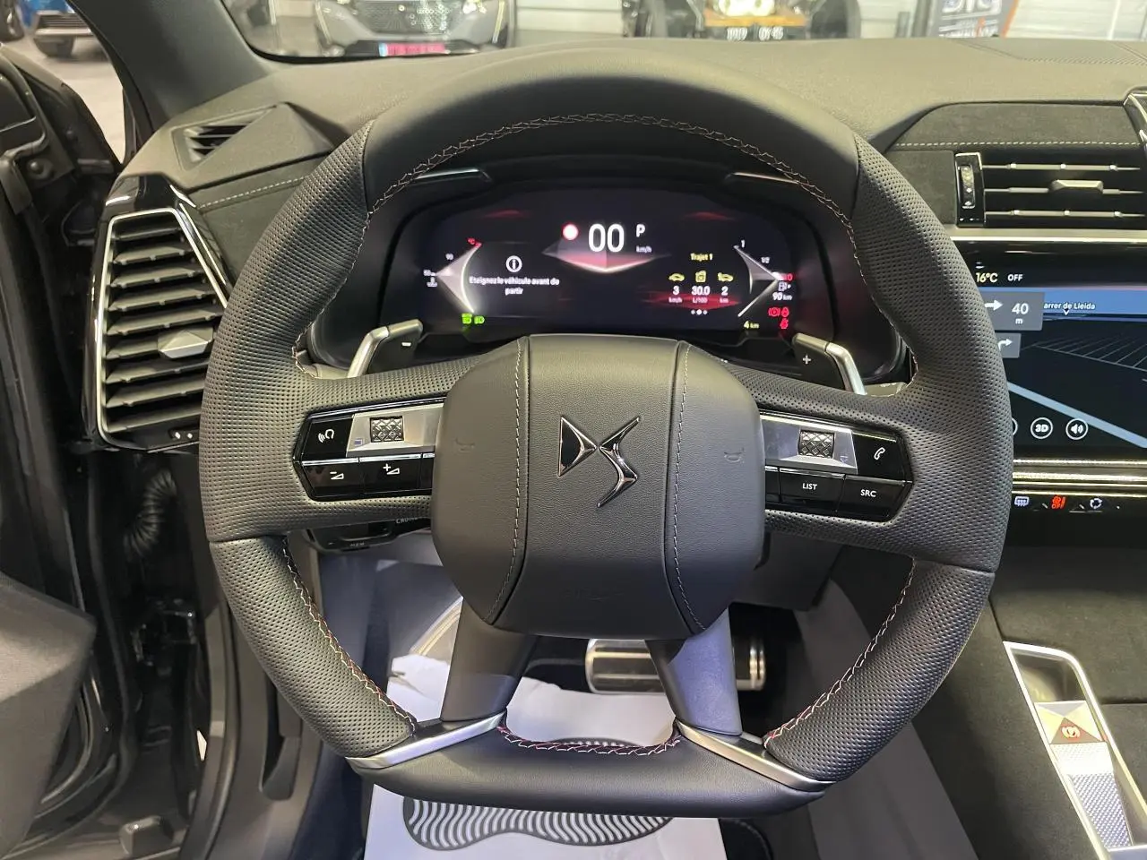 Vue rapprochée du volant en cuir perforé noir avec surpiqûres Carmin et Or du DS7 Crossback gris titanium, tableau de bord numérique visible.