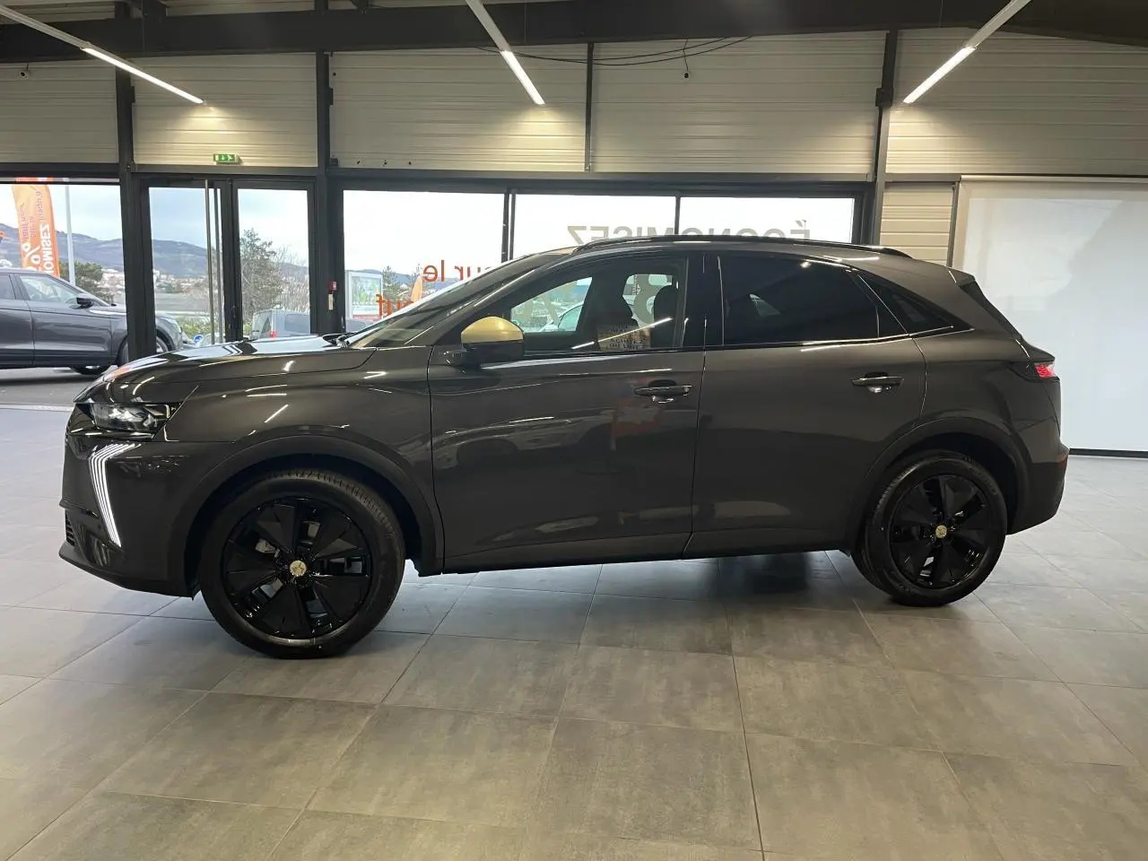 Vue latérale droite du DS7 Crossback gris titanium avec jantes noires et coques de rétroviseurs dorées satinées en intérieur showroom.