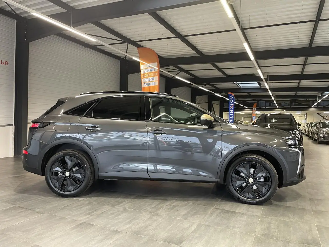 Vue latérale droite d'un DS7 Crossback gris titanium avec jantes noires et vitres arrière surteintées en intérieur showroom.
