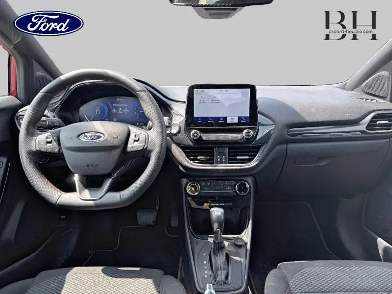 Vue frontale de l'habitacle du Ford Puma rouge, mettant en valeur le volant sport multifonction et l'écran tactile central.
