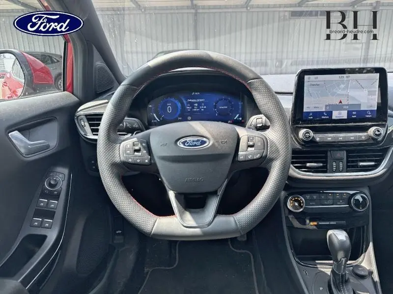 Vue intérieure du poste de conduite de la Ford Puma rouge, avec volant multifonction et écran tactile central.