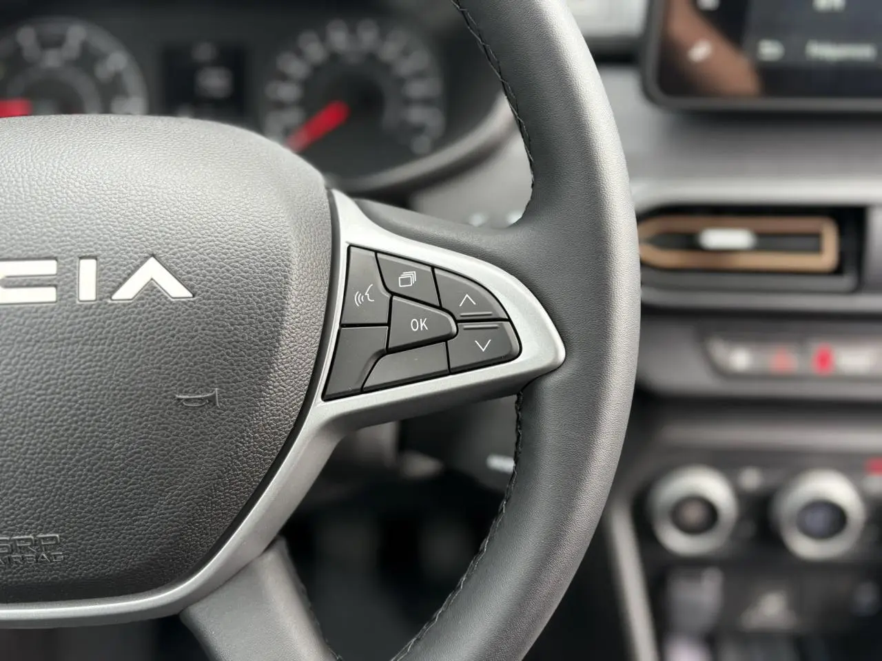 Gros plan sur le volant noir de la Dacia Jogger 2025 avec commandes intégrées et tableau de bord flou en arrière-plan.