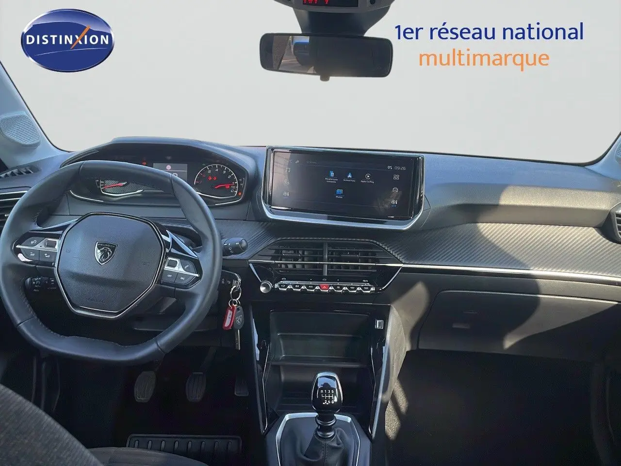 Vue intérieure avant du tableau de bord de la Peugeot 208 blanc banquise 2024 avec volant multifonction et boîte manuelle.