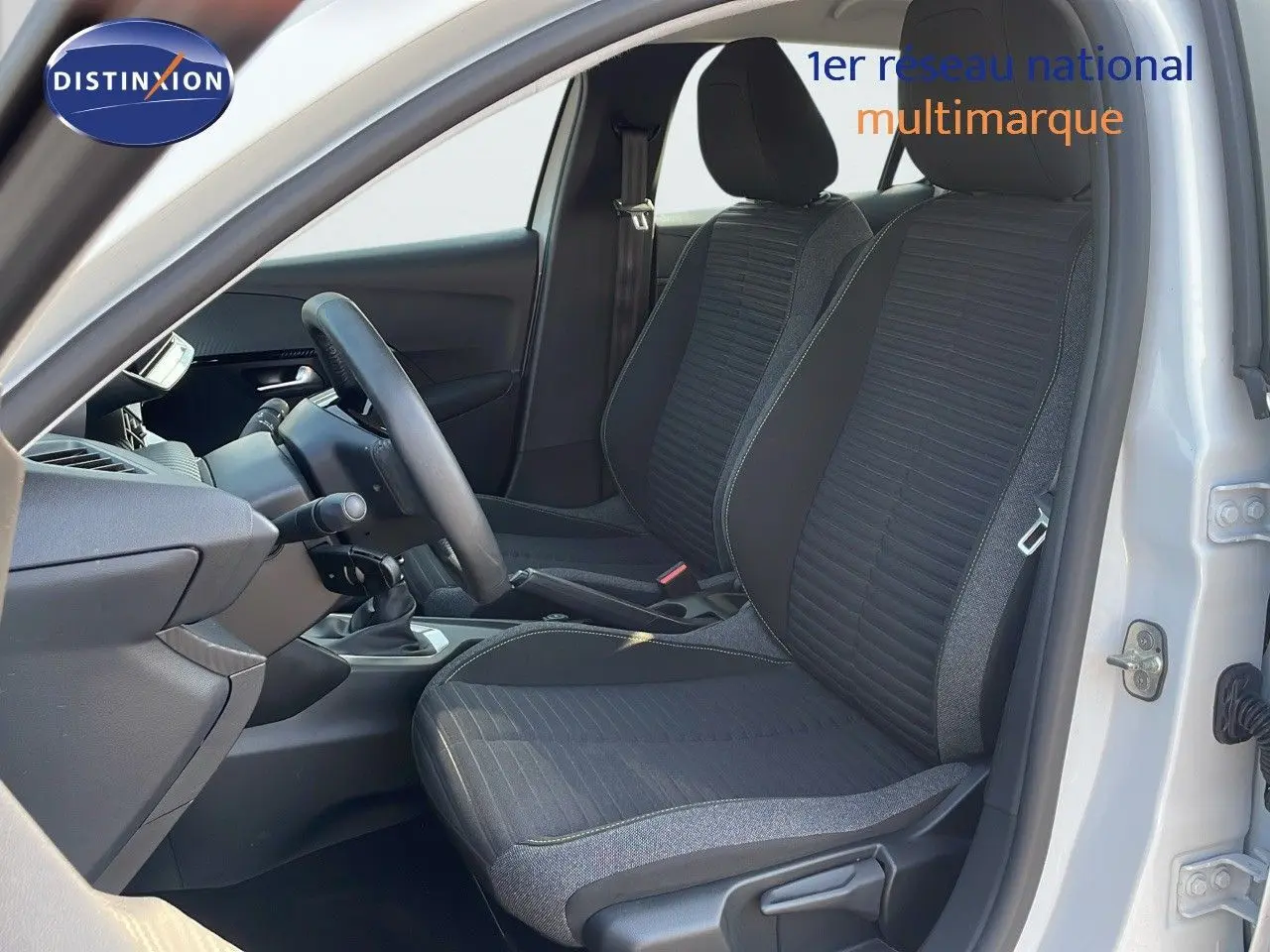 Vue intérieure côté conducteur de la Peugeot 208 blanche, montrant les sièges noirs et la console avec boîte manuelle.