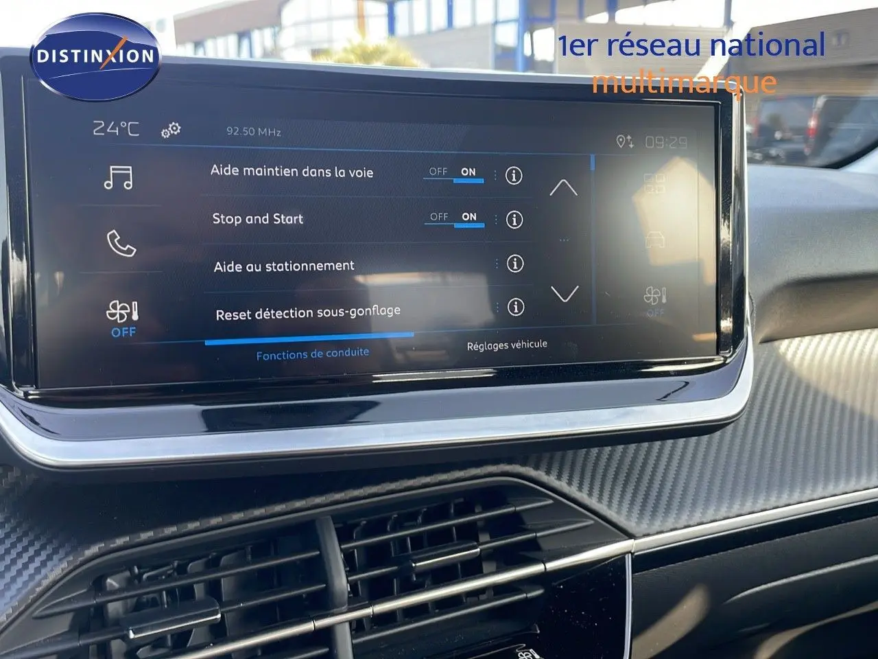 Vue rapprochée de l'écran tactile central du tableau de bord d'une Peugeot 208 blanche, affichant les aides à la conduite.