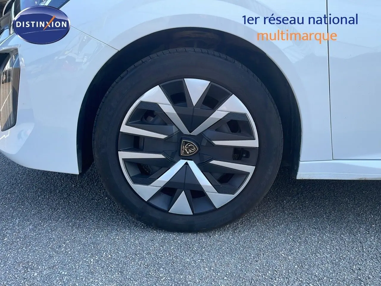 Gros plan sur la roue avant gauche d’une Peugeot 208 blanche Banquise 2024 avec jante au design géométrique noir et argent.