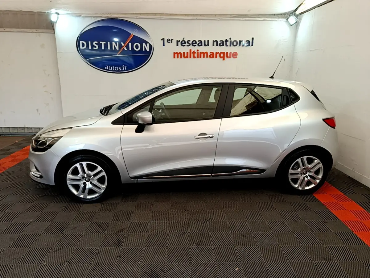 Profil côté gauche d'une Renault Clio Business TCe 90 gris clair, en intérieur avec logo Distinxion en arrière-plan.