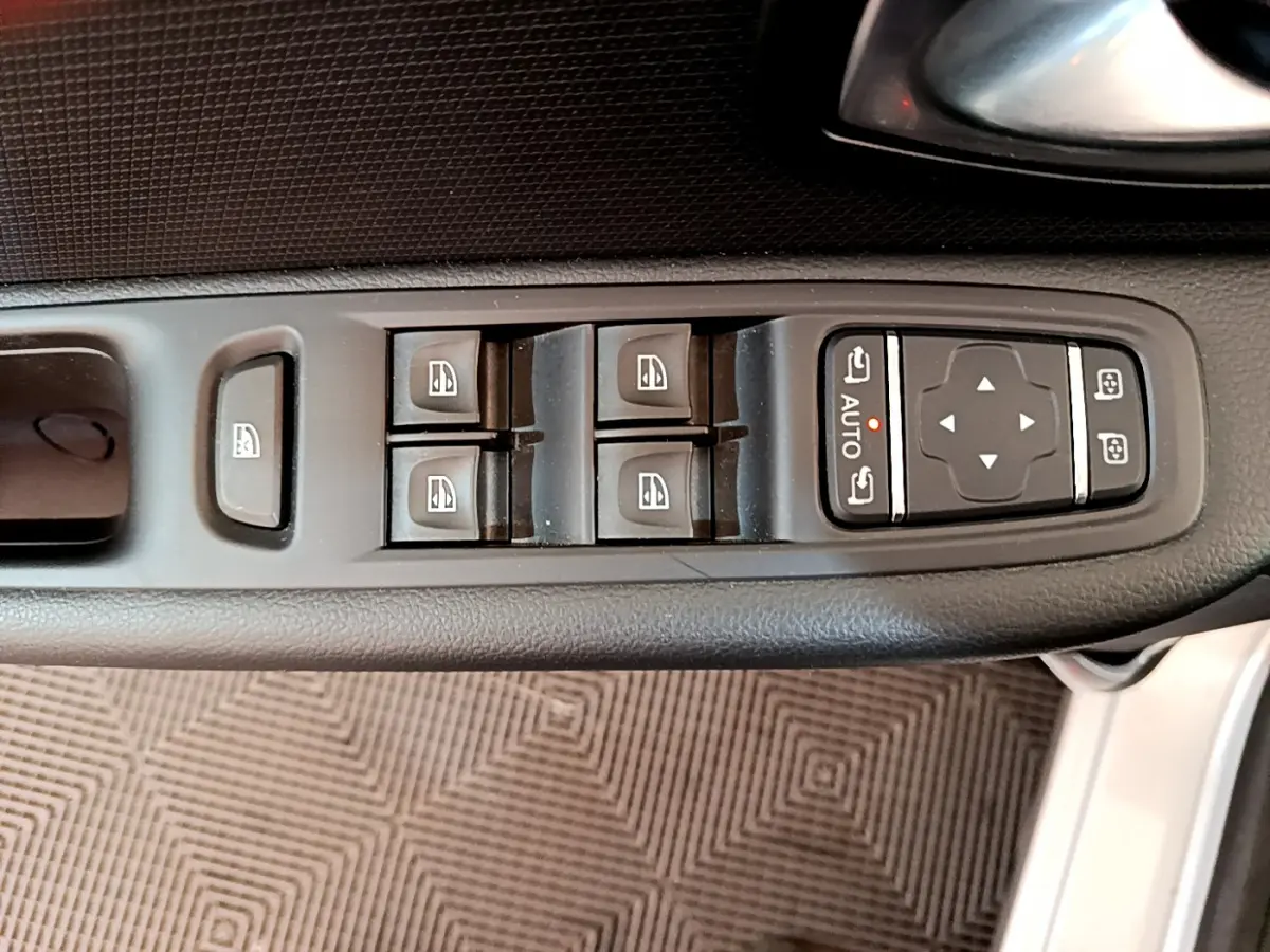 Vue rapprochée des commandes de lève-vitres et réglage des rétroviseurs côté conducteur d'une Renault Clio gris clair 2019.