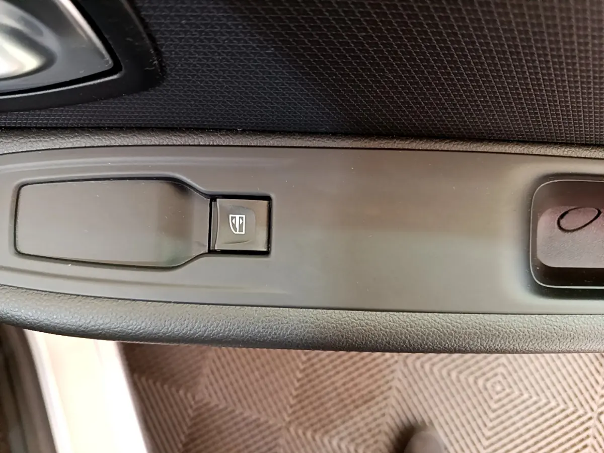 Gros plan sur le bouton de commande de la vitre électrique côté conducteur de la Renault Clio Business gris clair.