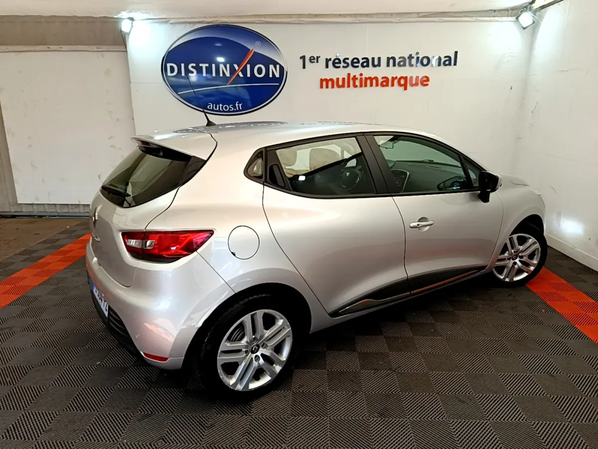Renault Clio Business TCe 90 gris clair vue 3/4 arrière droit dans un showroom avec logo Distinxion en arrière-plan.
