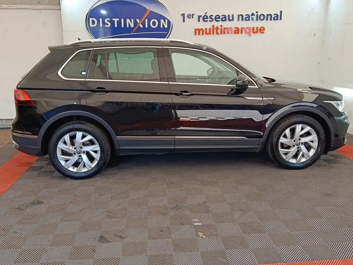 Vue latérale droite d'un Volkswagen Tiguan noir 2022 avec jantes alliage et rails de toit chromés en intérieur showroom.