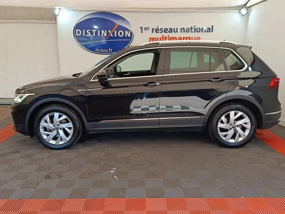 Vue de profil côté gauche d’un Volkswagen Tiguan noir 2022, avec jantes alliage et barres de toit chromées.