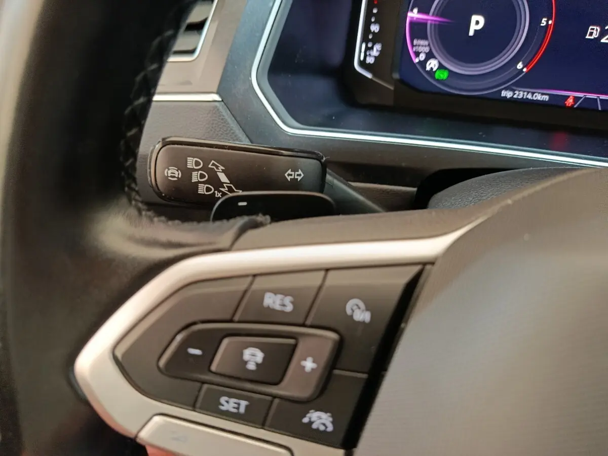 Gros plan sur le volant noir du Volkswagen Tiguan 2022, avec commandes du régulateur adaptatif et tableau de bord numérique.
