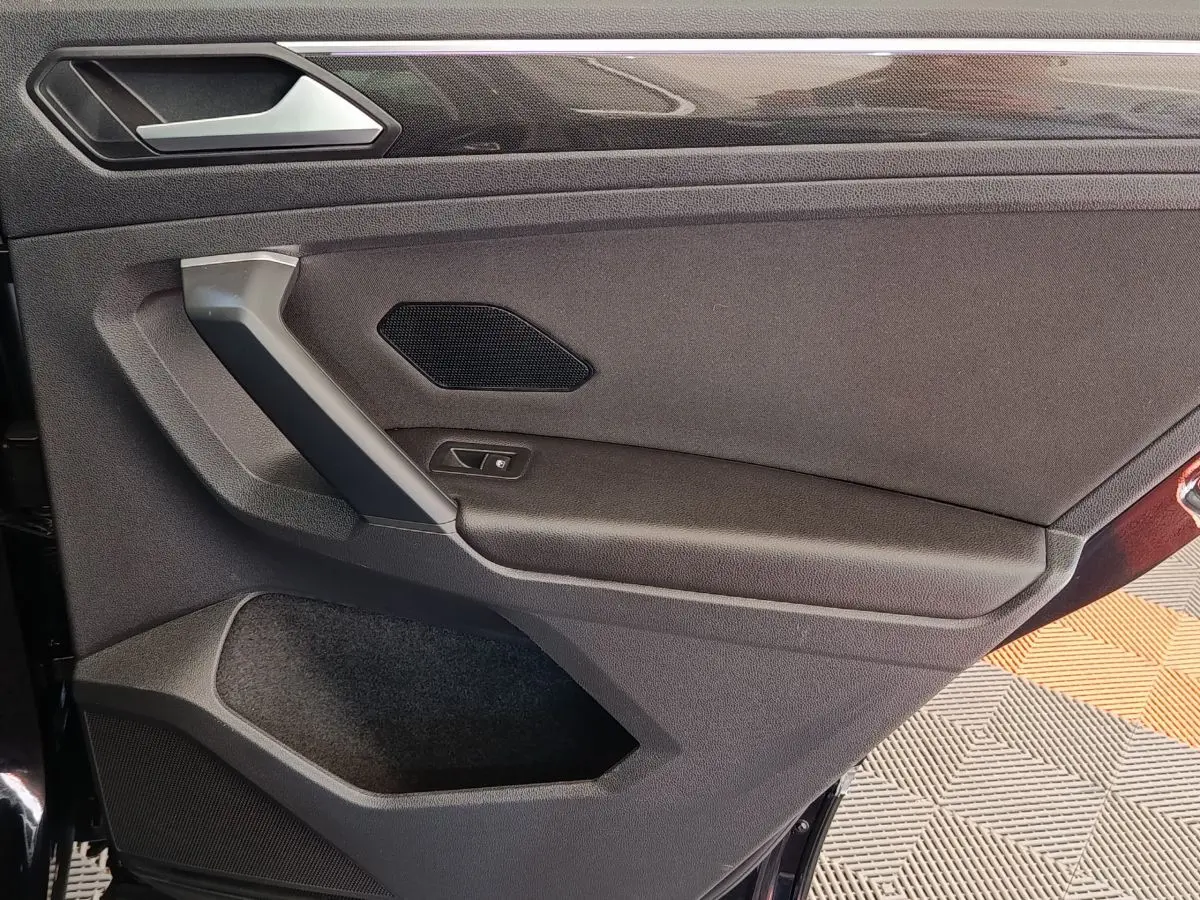 Vue intérieure côté gauche de la porte arrière noire du Volkswagen Tiguan 2.0 TDI avec poignée et haut-parleur intégrés.