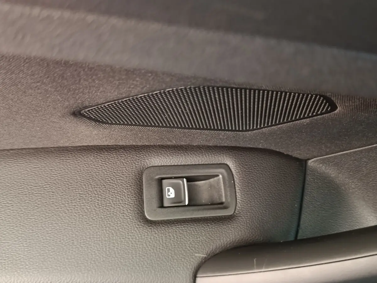Détail intérieur du bouton d'ouverture électrique du coffre sur la porte arrière d'un Volkswagen Tiguan noir.