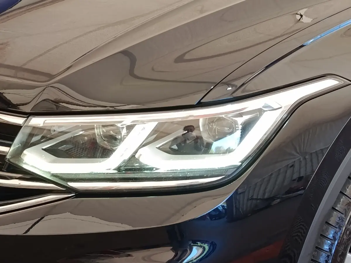 Gros plan sur le phare avant droit allumé du Volkswagen Tiguan noir 2022, soulignant ses LED distinctives.