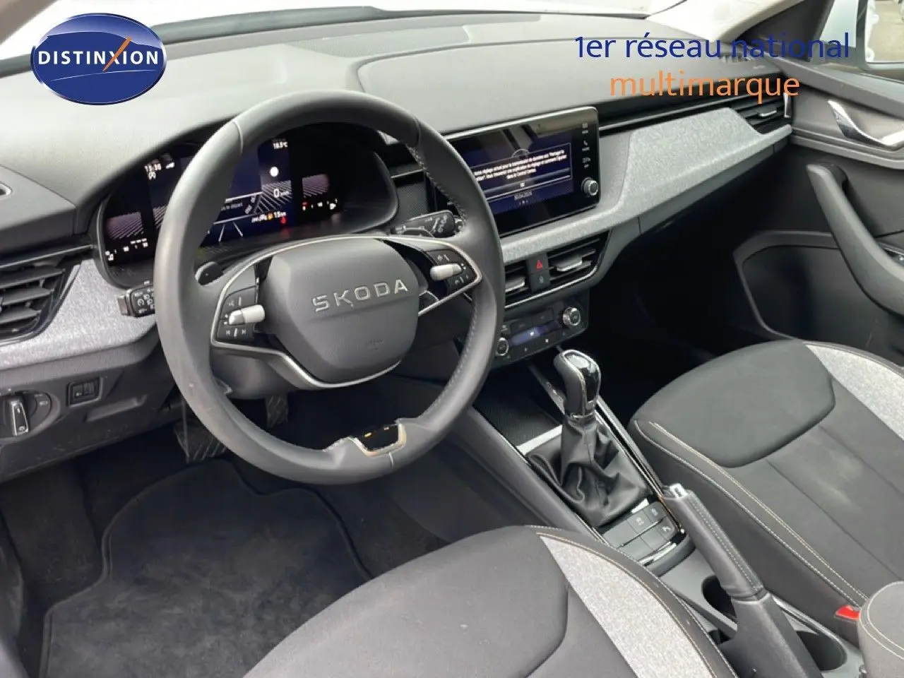 Vue intérieure avant du Skoda Kamiq blanc glacier, mettant en valeur le volant multifonction et la console centrale avec boîte automatique.