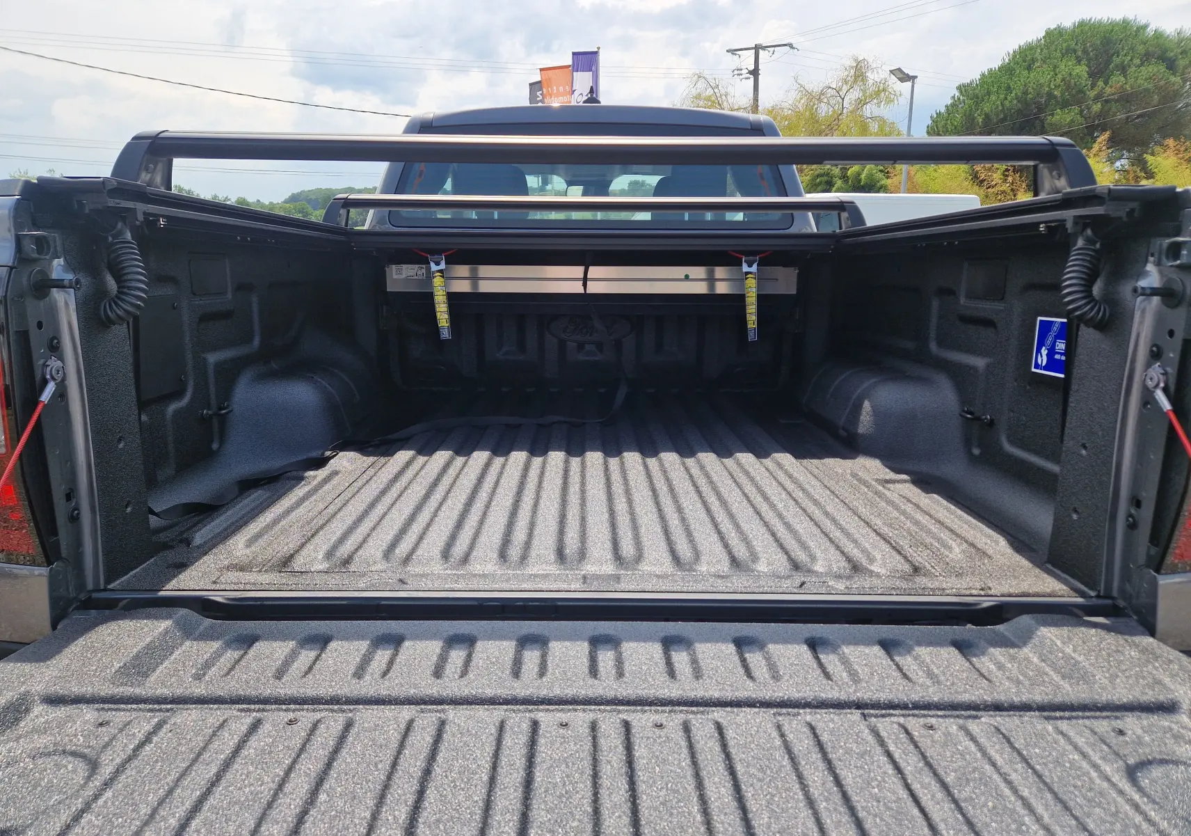 Vue arrière du plateau ouvert du Ford Ranger Super Cabine gris carbone, avec rideau rigide coulissant et protection renforcée.