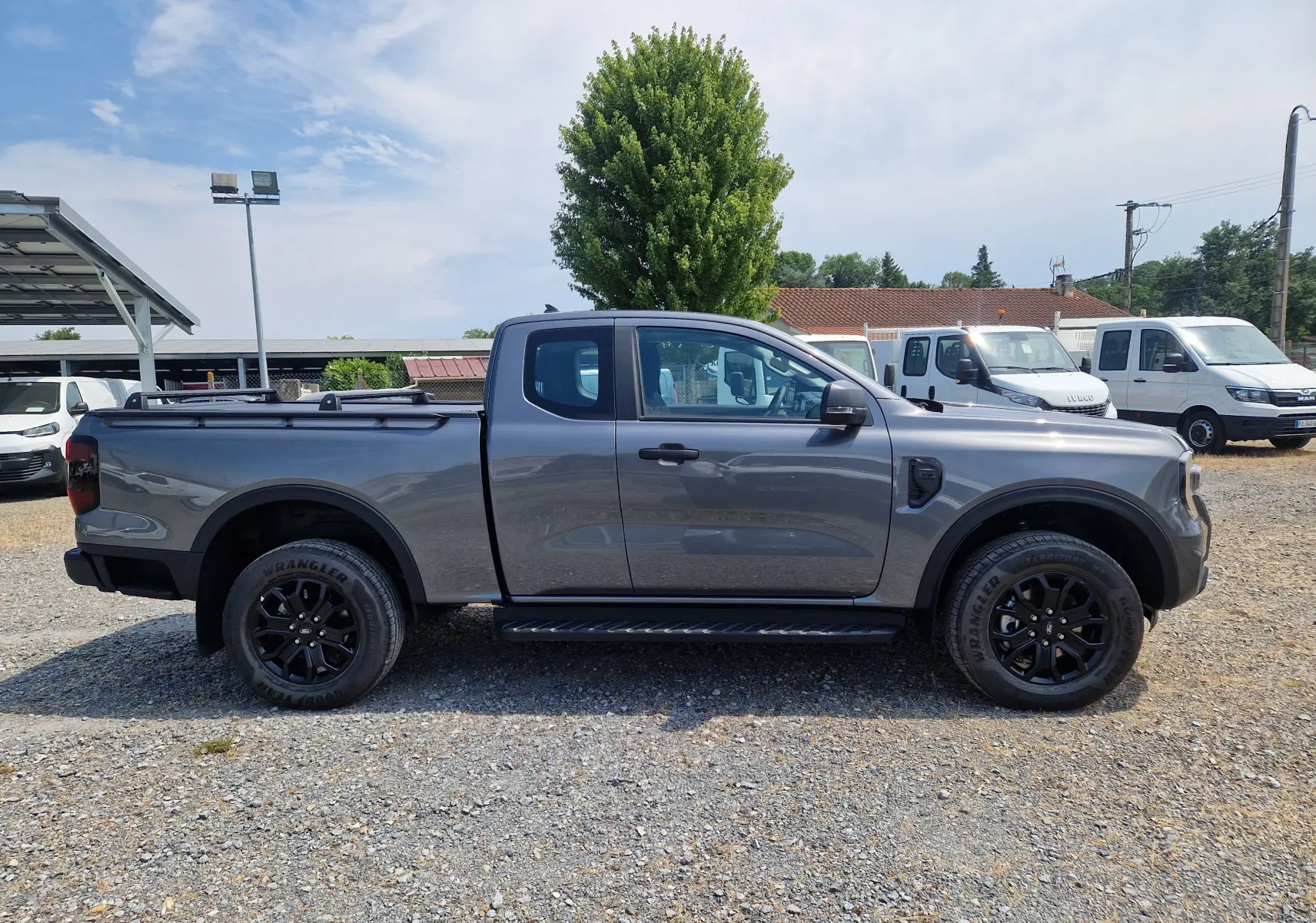 Ford Ranger Super Cabine gris carbone vu de profil côté gauche, avec marchepied et rideau de plateau rigide coulissant.
