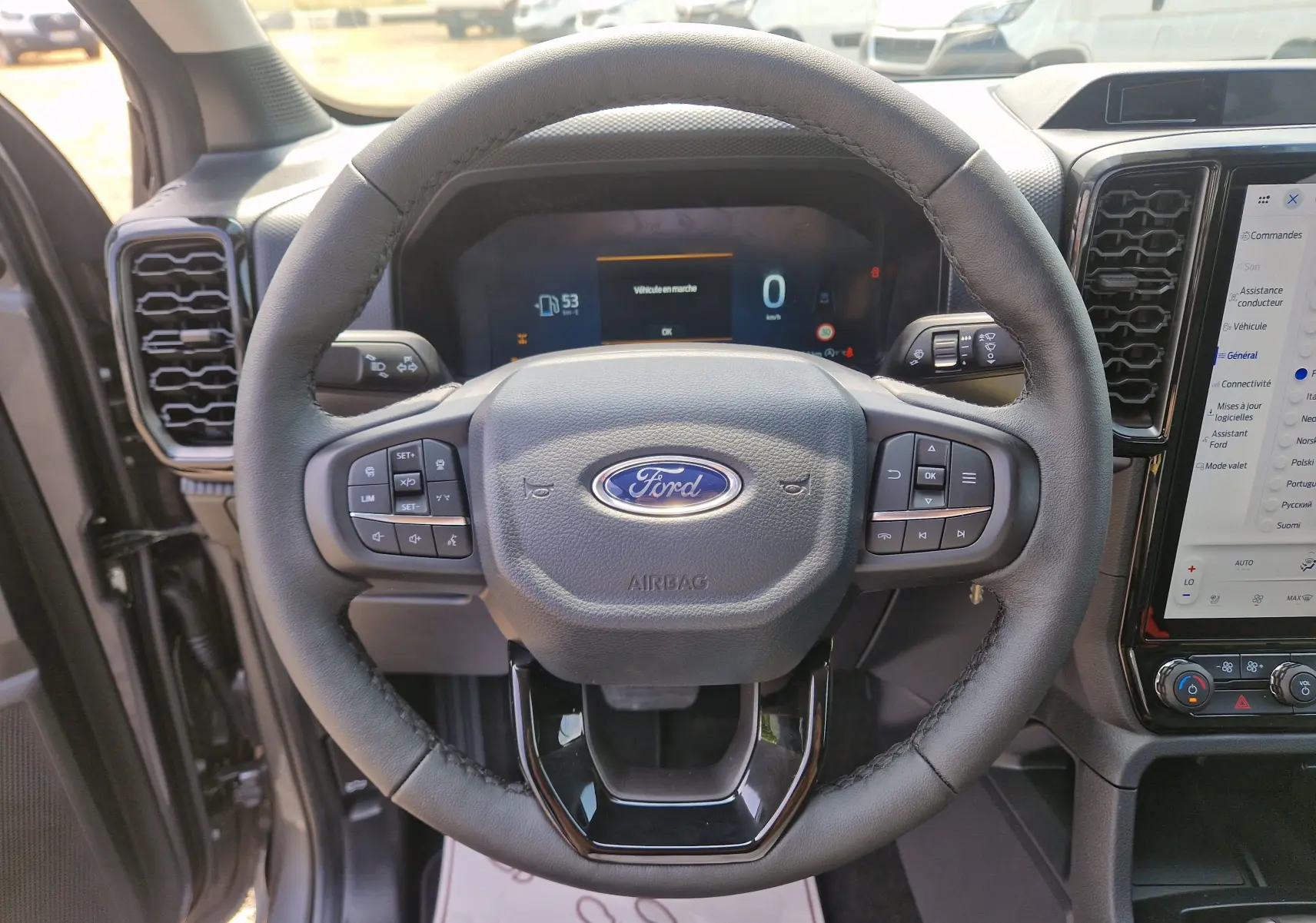 Vue rapprochée du volant noir du Ford Ranger Super Cabine gris carbone, avec tableau de bord numérique et écran tactile visible.