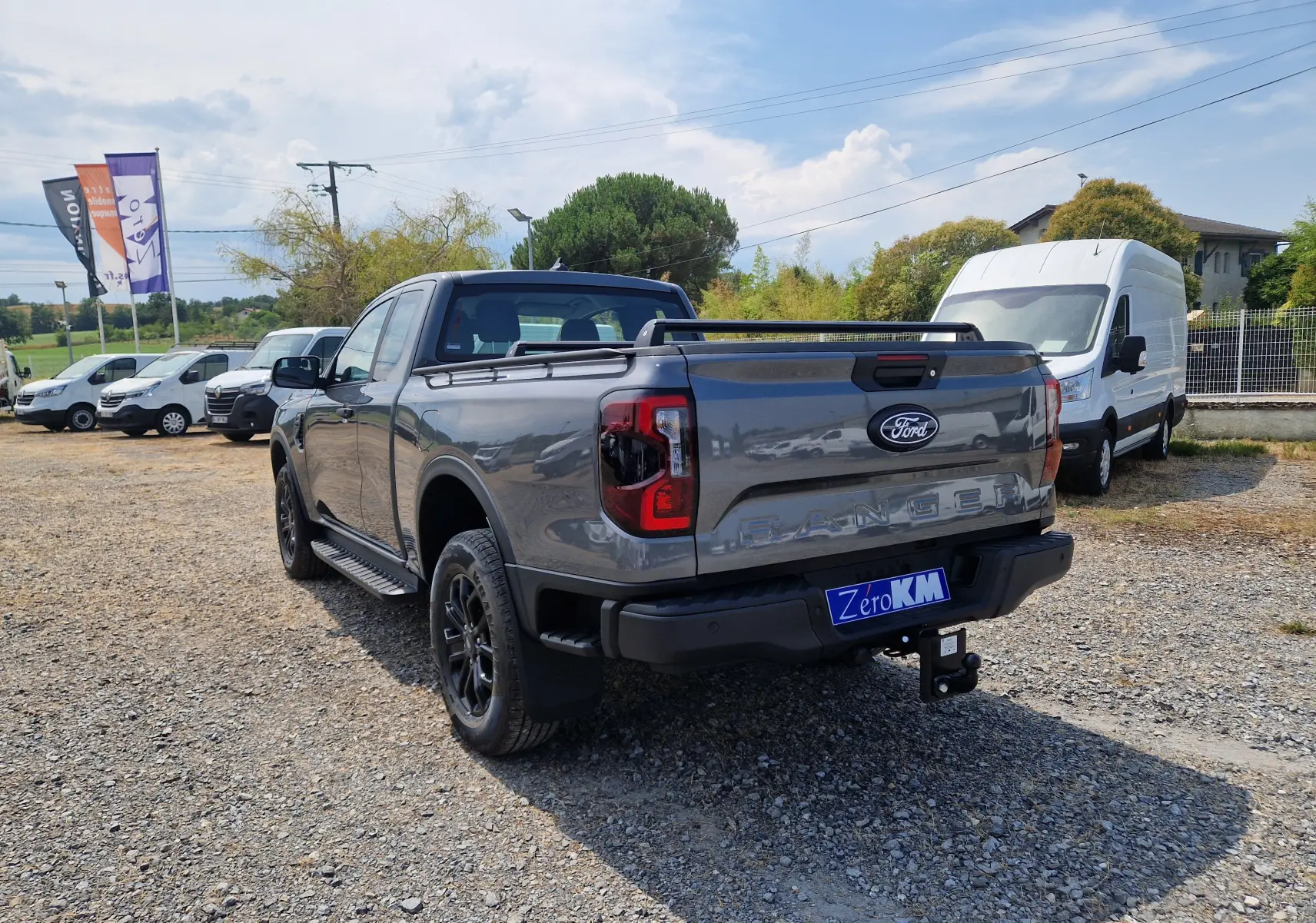 Vue 3/4 arrière droite du Ford Ranger Super Cabine gris carbone avec rideau de plateau rigide et barres sur le toit.