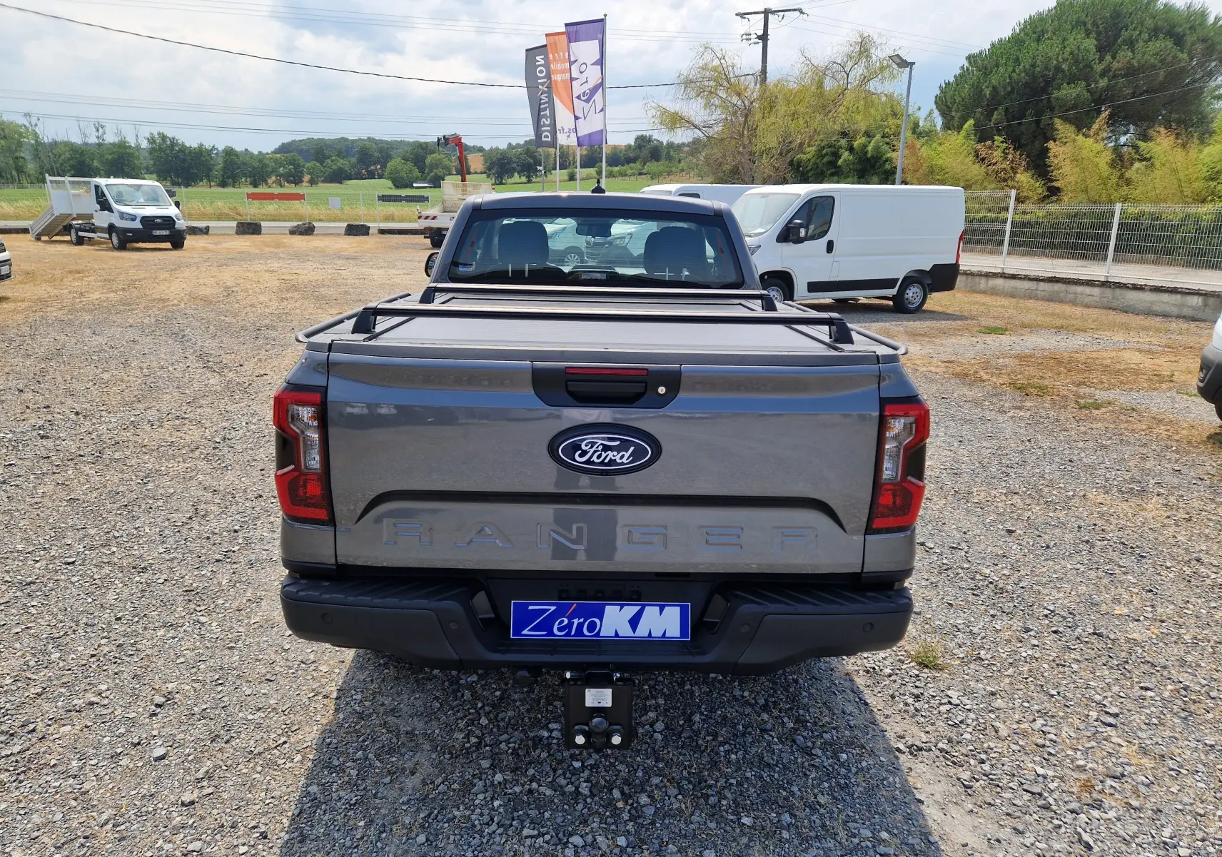 Vue arrière d'un Ford Ranger Super Cabine gris carbone avec rideau de plateau rigide et attelage visible.