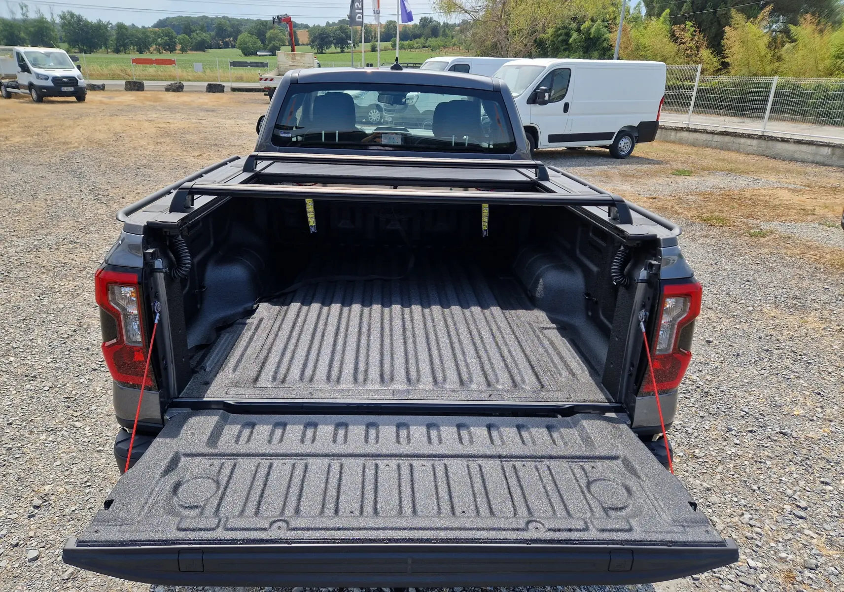 Vue arrière du Ford Ranger Super Cabine gris carbone avec plateau ouvert et rideau rigide coulissant visible.
