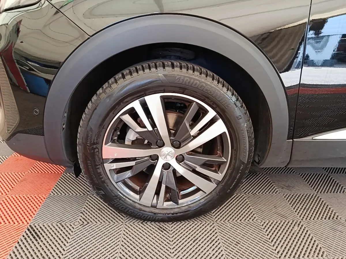 Gros plan sur la roue avant gauche noire du Peugeot 3008 PureTech 130 Allure, jante alliage bicolore.
