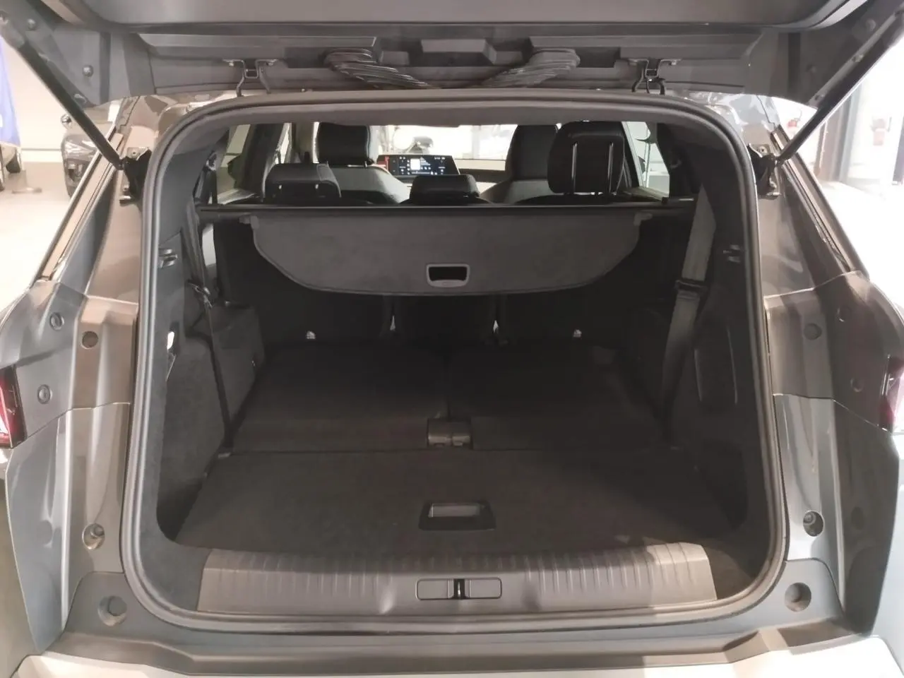 Coffre ouvert vu de l'arrière d'un Peugeot 5008 gris titanium avec banquette arrière rabattue et cache-bagages déployé.