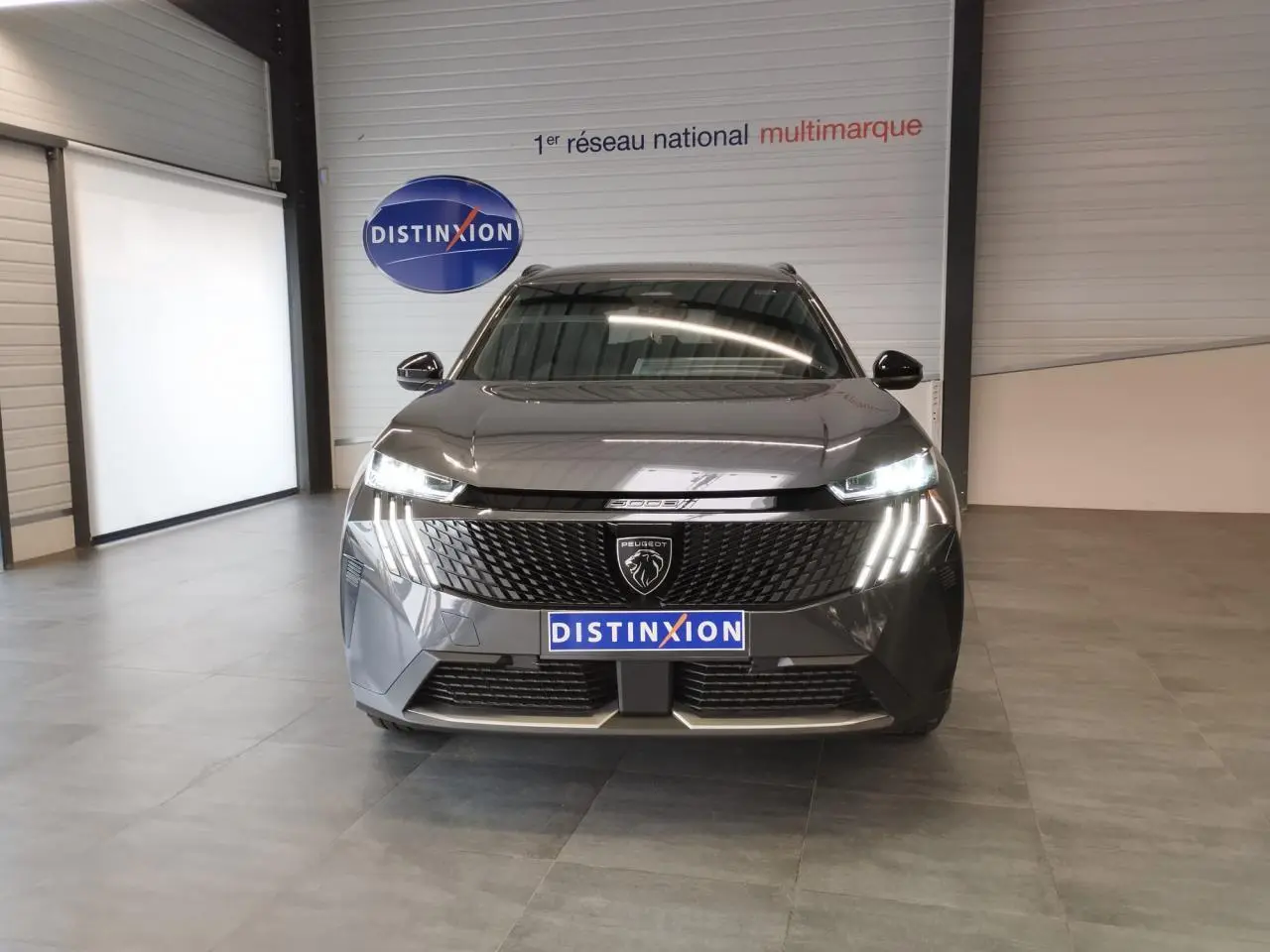 Peugeot 5008 gris titanium vue de face en intérieur, avec calandre noire et feux LED 3 griffes allumés.