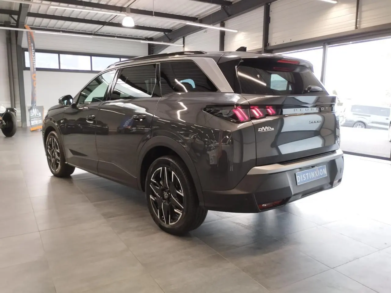 Peugeot 5008 gris titanium vue 3/4 arrière droit en intérieur avec feux arrière LED 3 griffes allumés.