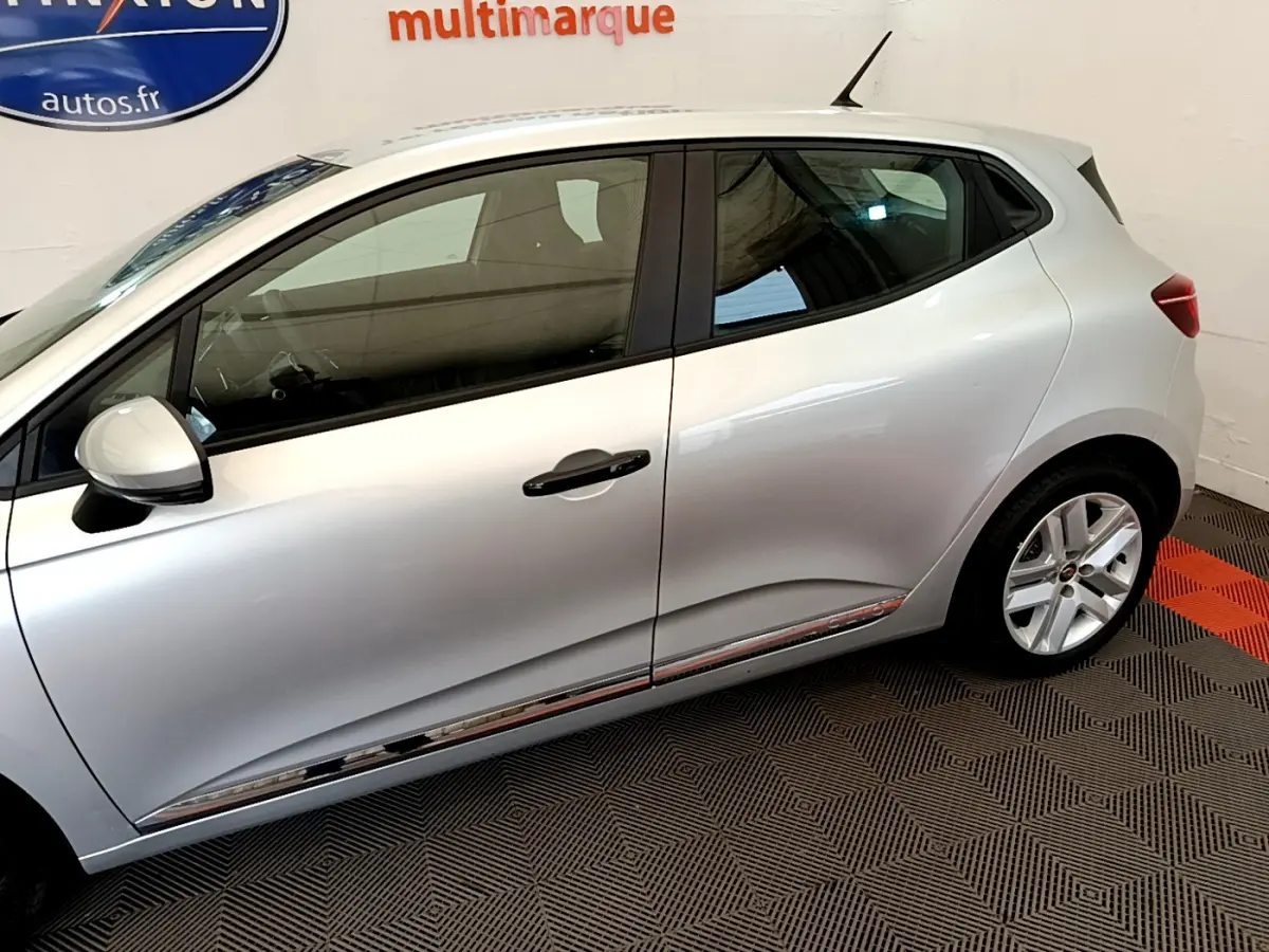 Profil côté gauche d'une Renault Clio Business TCe 100 gris clair, soulignant la ligne de caisse chromée et les jantes alliage.