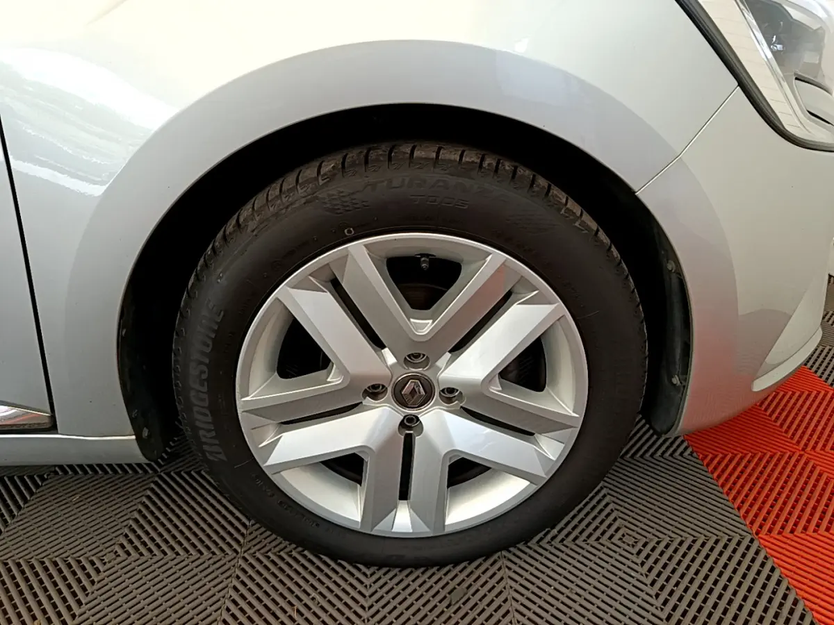 Gros plan sur la roue avant droite d'une Renault Clio gris clair, mettant en valeur la jante alliage et le logo central.