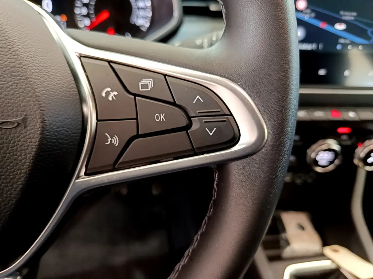 Gros plan sur les commandes du volant en cuir synthétique de la Renault Clio Business TCe 100, tableau de bord flou en arrière-plan.