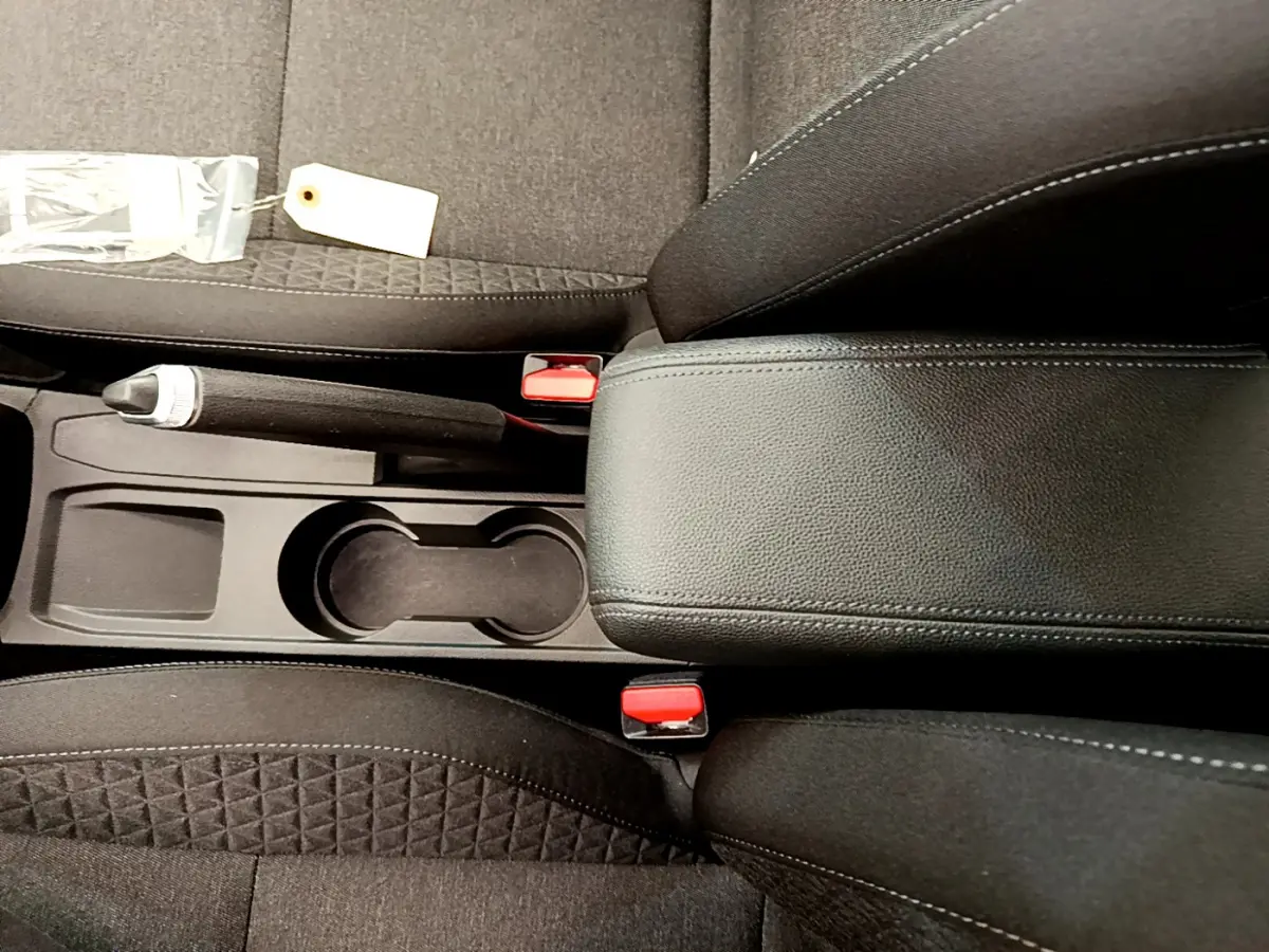 Vue plongeante sur la console centrale noire de la Renault Clio Business TCe 100 avec frein à main manuel et accoudoir cuir.