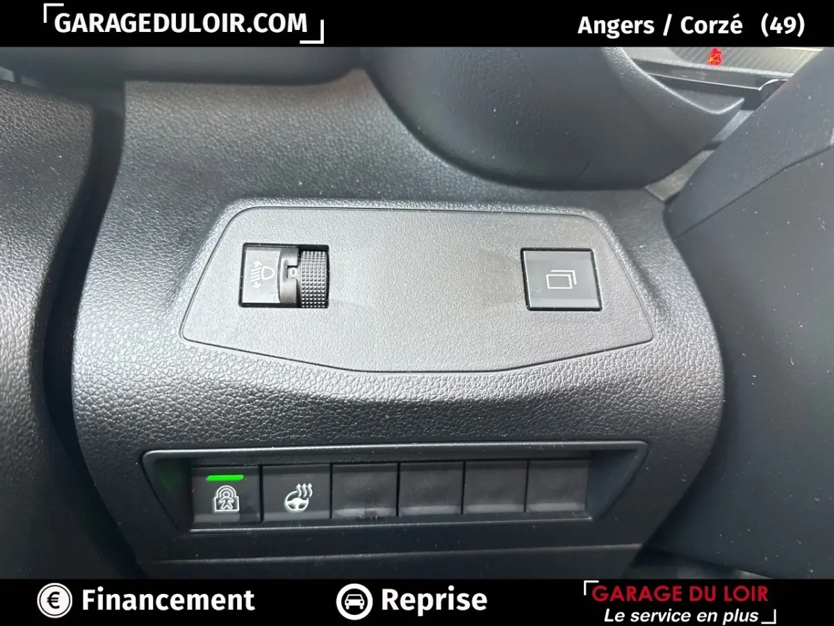 Gros plan sur les commandes noires du tableau de bord du Citroën Berlingo gris clair, avec réglage des phares et bouton de verrouillage.