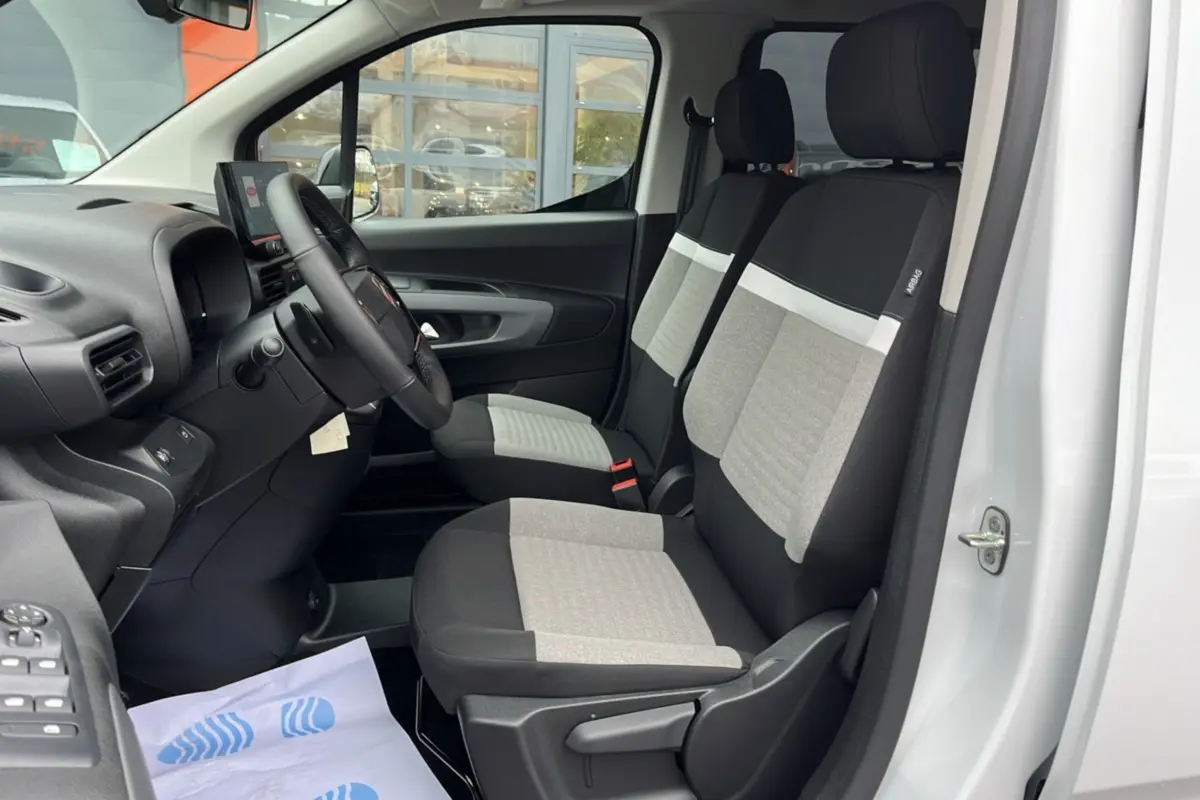 Vue intérieure côté conducteur du Citroën Berlingo blanc Kaolin, montrant les sièges tissu bicolores et le volant multifonctions.