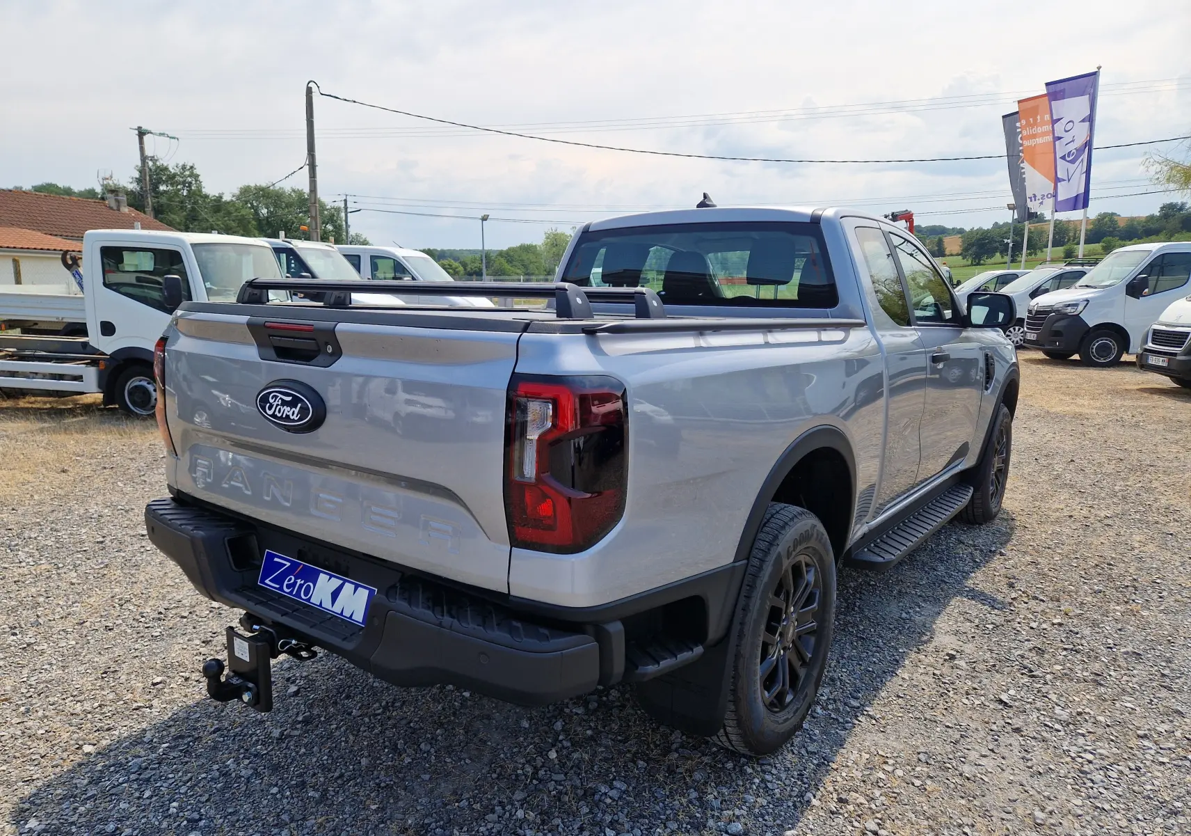Vue 3/4 arrière droite du Ford Ranger Super Cabine gris Iconic avec ridelle coulissante et barres de plateau visibles.