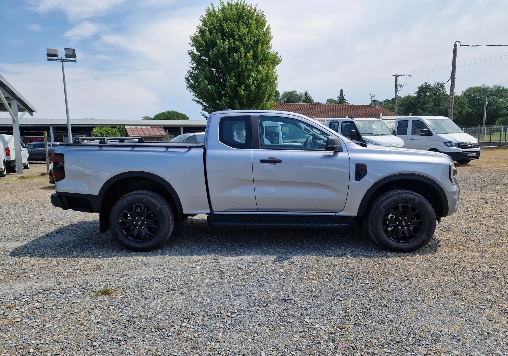 Ford Ranger Super Cabine gris iconic vu de profil côté gauche, avec marchepied et barres sur plateau.