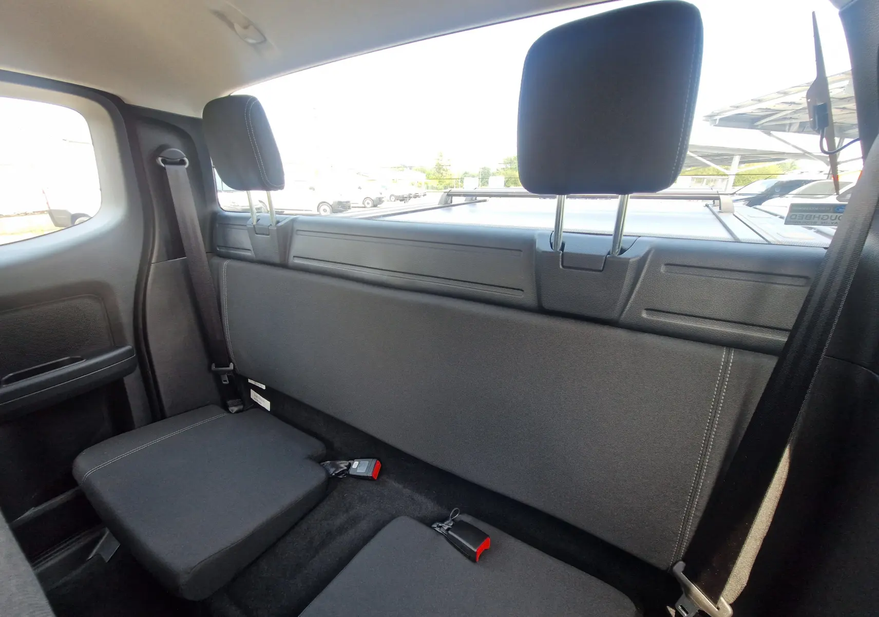 Vue intérieure arrière du Ford Ranger Super Cabine gris Iconic, montrant les sièges rabattus et la fenêtre arrière.