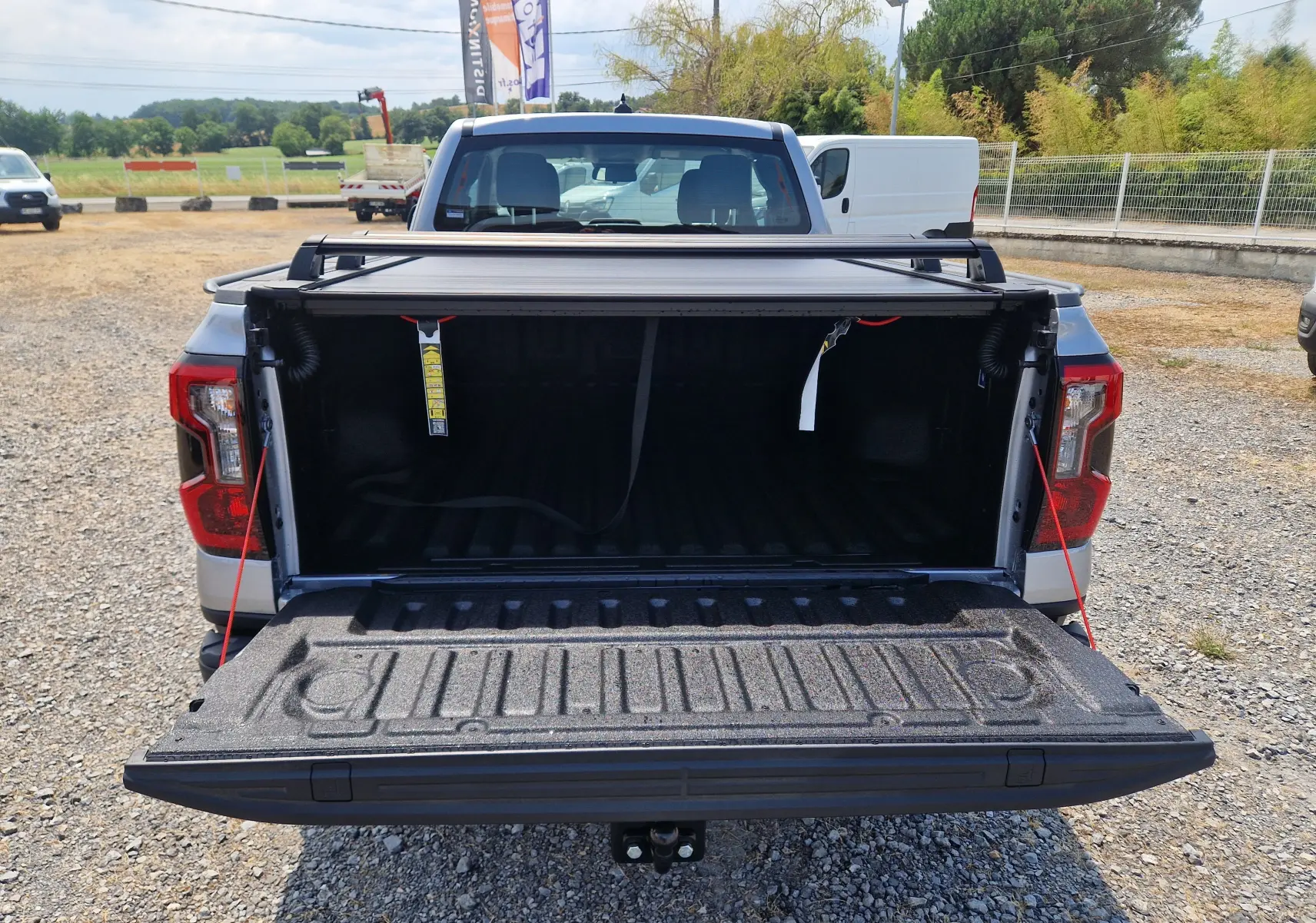 Vue arrière d'un Ford Ranger Super Cabine gris Iconic avec plateau ouvert et rideau rigide coulissant visible.