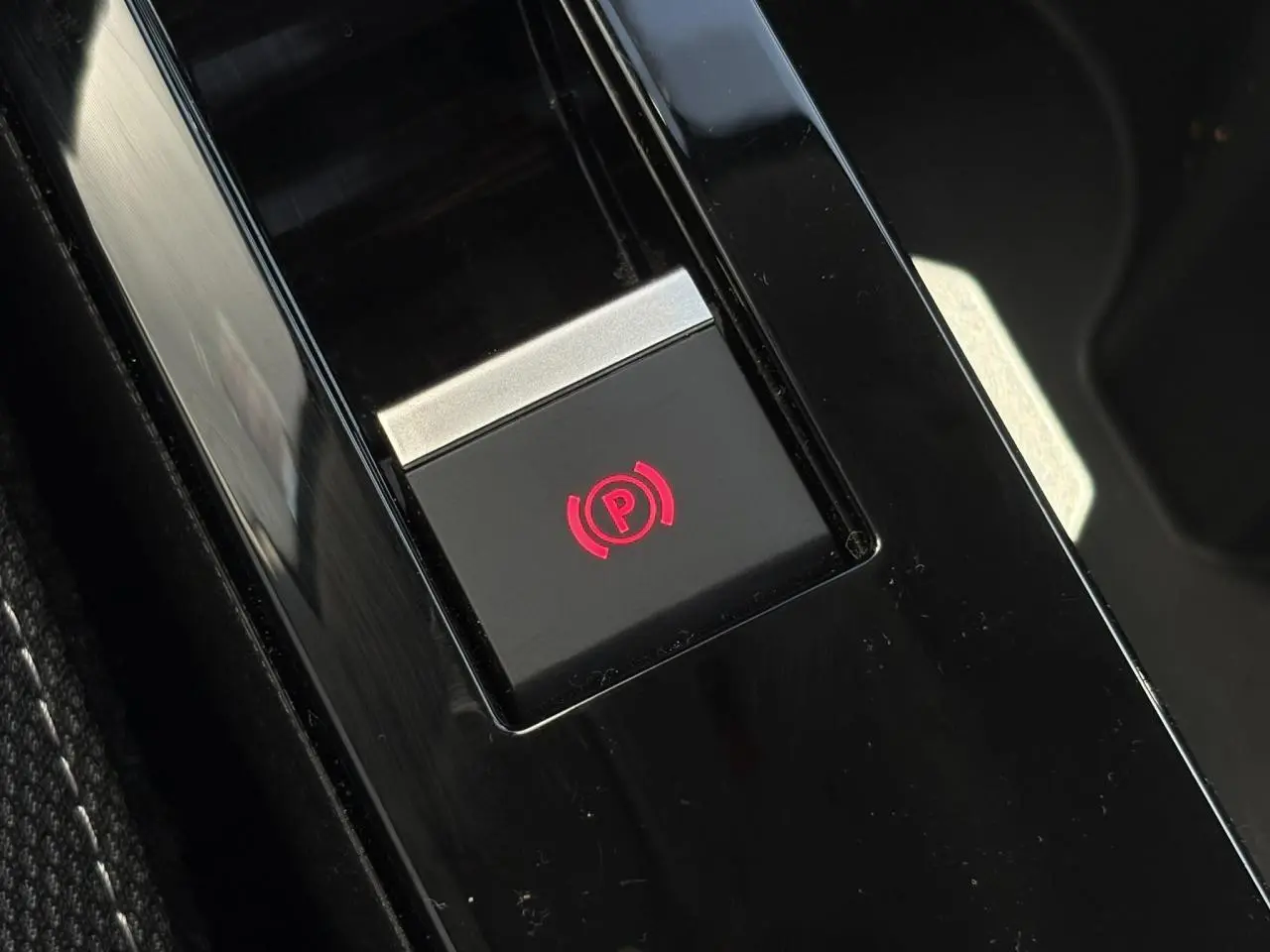 Gros plan sur le bouton de frein de stationnement électrique rouge, console centrale noire de la Citroën C4 Hybrid 2025.