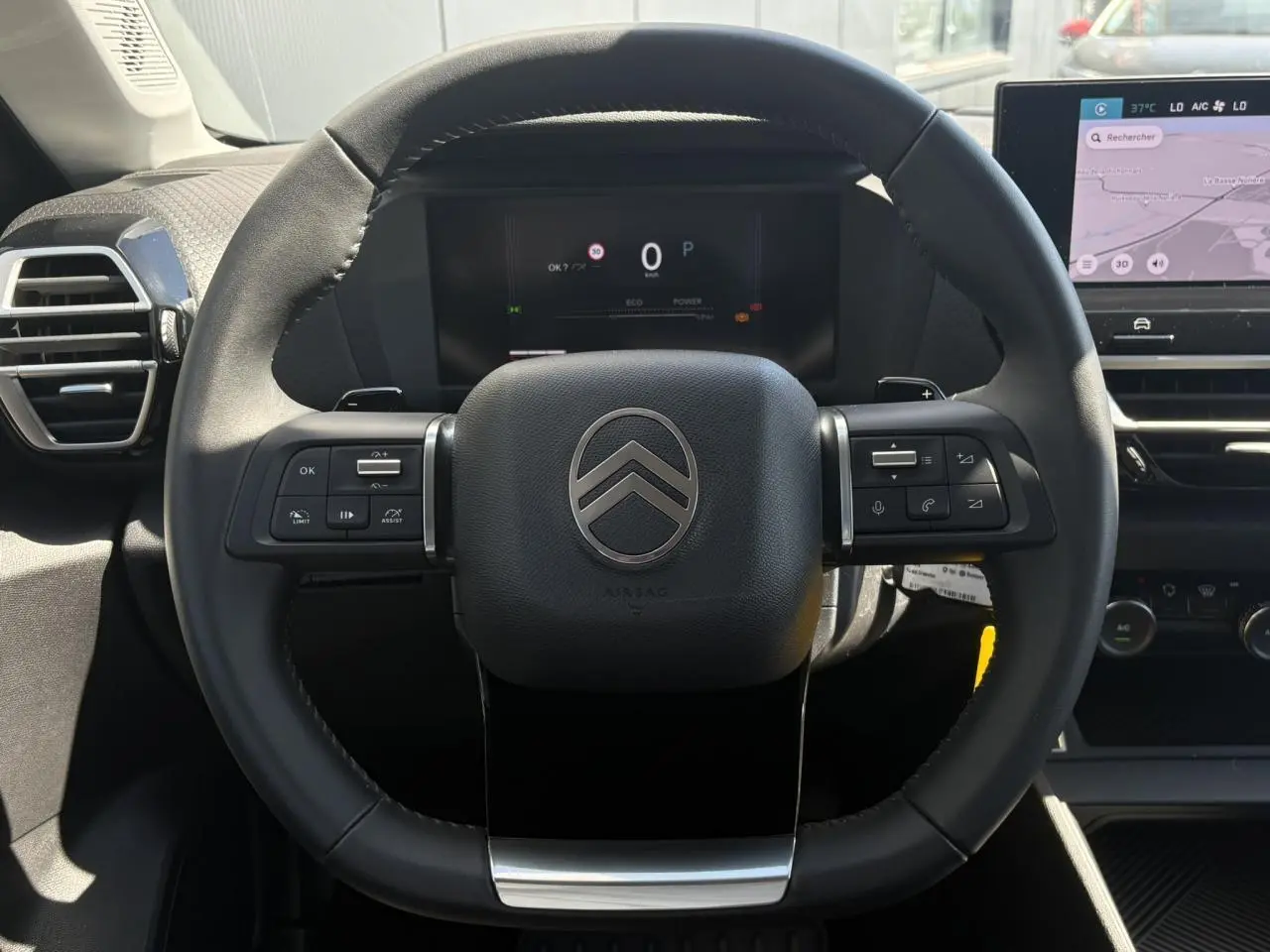 Vue rapprochée du volant cuir noir de la Citroën C4 Hybrid 2025 avec tableau de bord numérique et écran tactile.