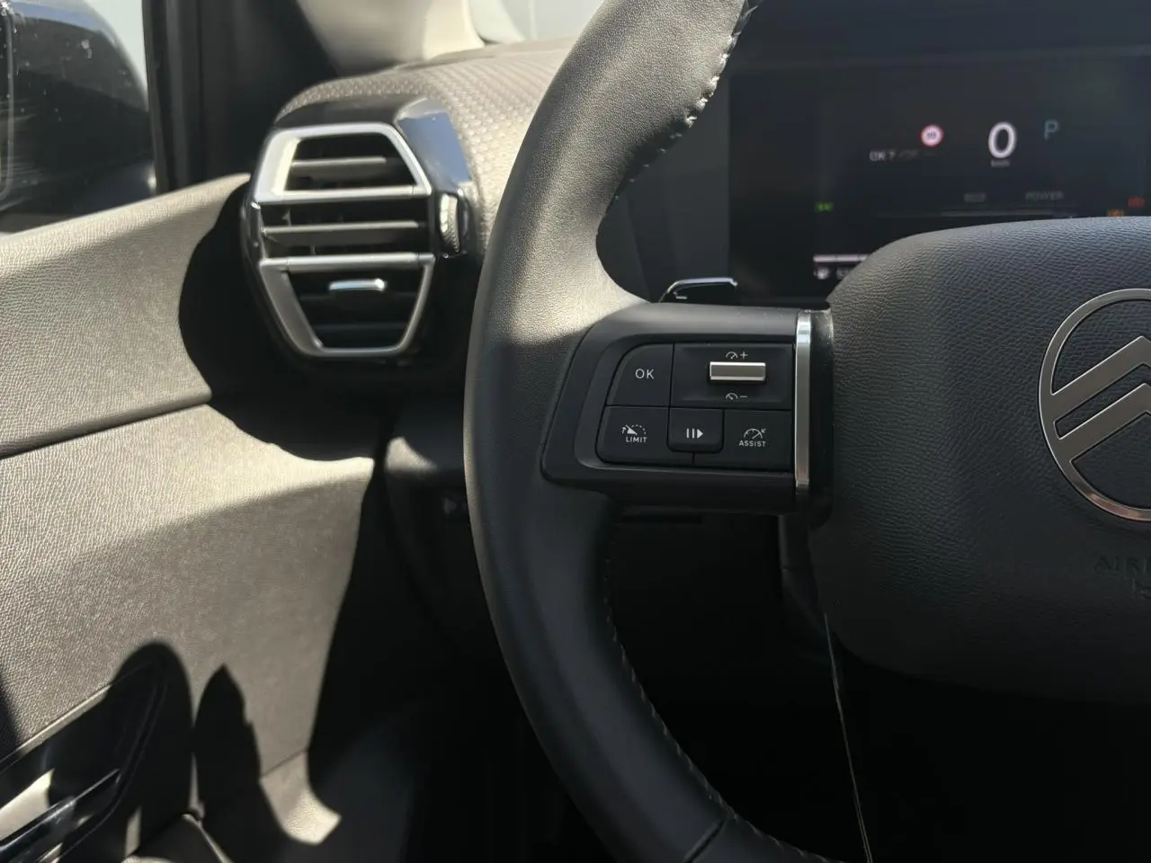 Gros plan sur le volant noir et les commandes à gauche du tableau de bord d'une Citroën C4 Hybrid 2025.