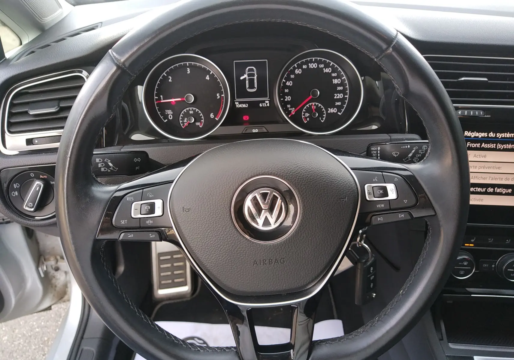 Vue rapprochée du volant noir de la Volkswagen Golf gris reflet d'argent, avec tableau de bord et commandes visibles.