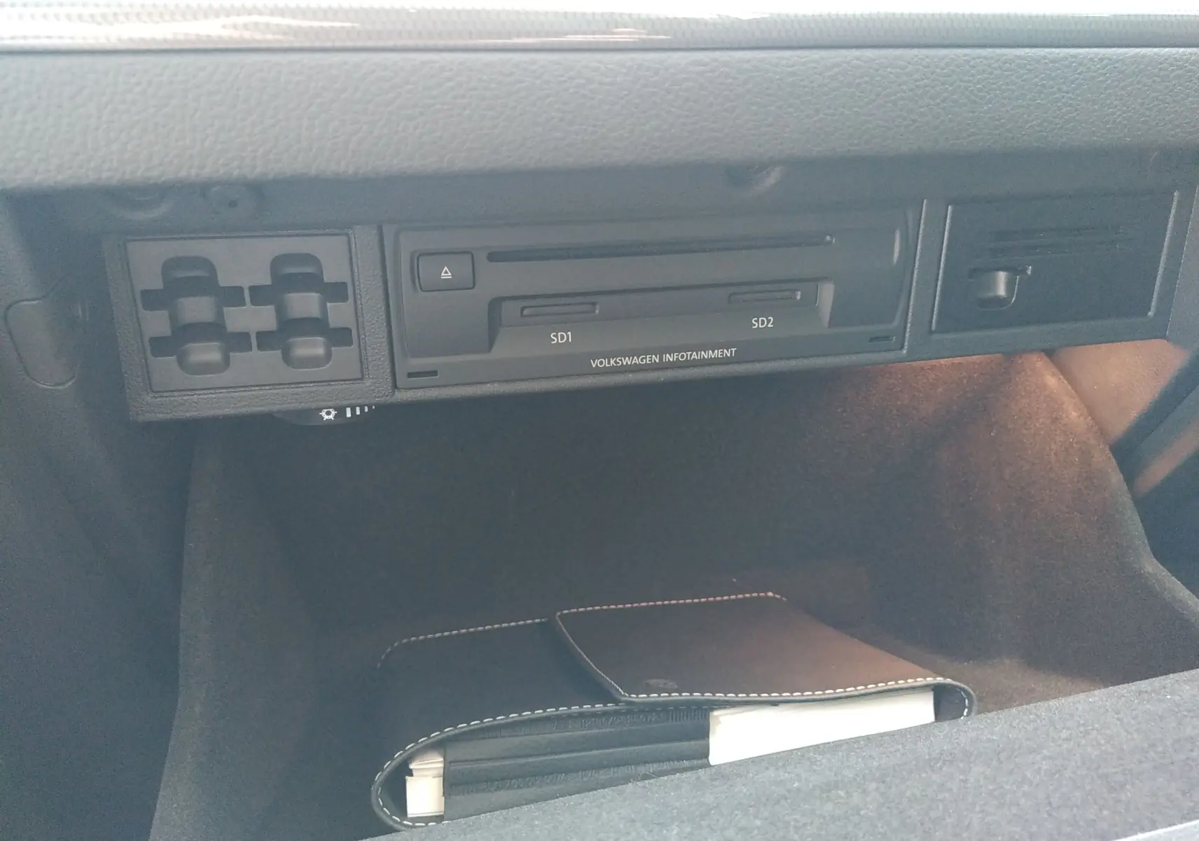 Vue rapprochée de la boîte à gants ouverte d’une Volkswagen Golf gris reflet d’argent, montrant le lecteur SD et un carnet noir.