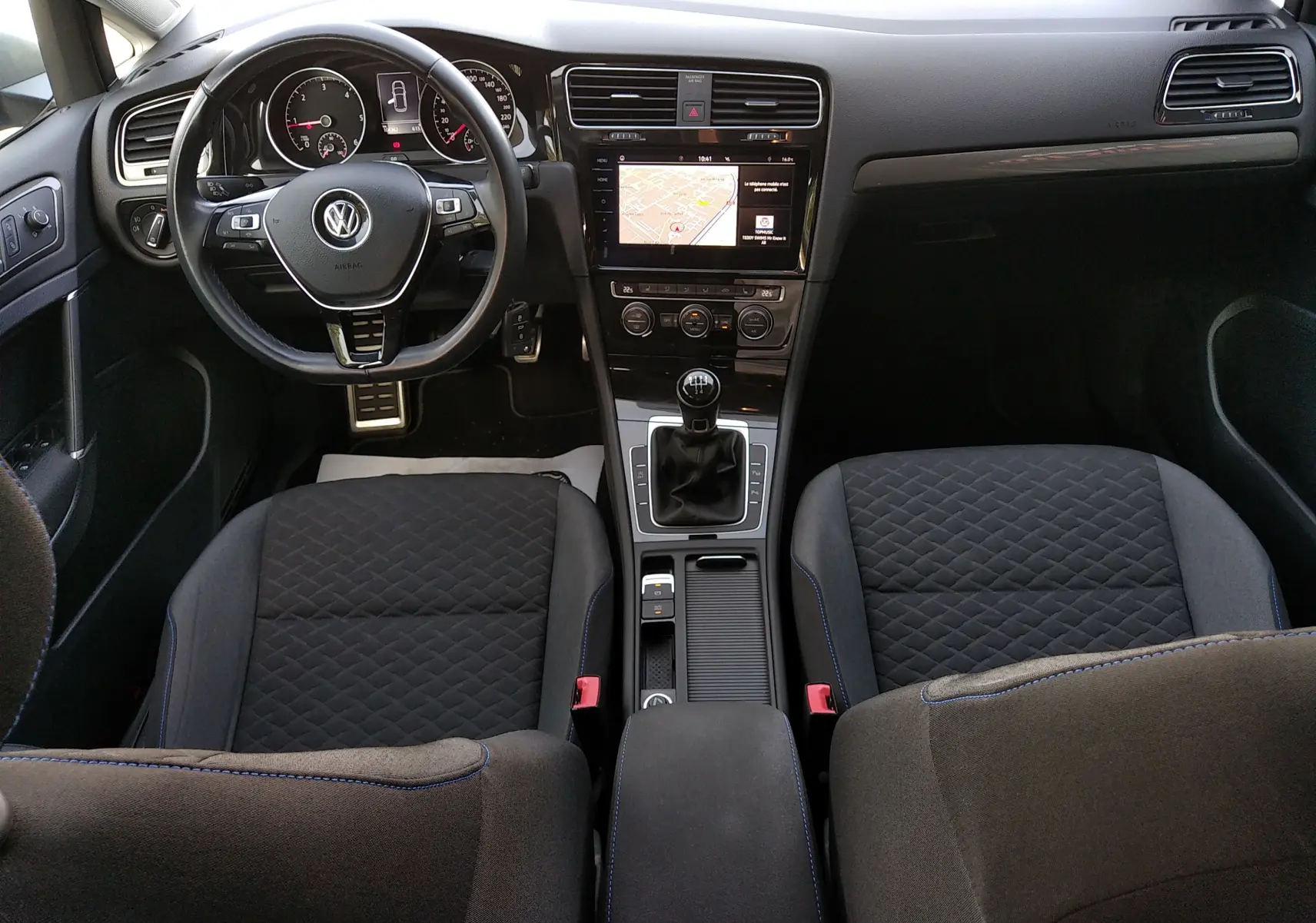 Vue intérieure avant de la Volkswagen Golf 1.6 TDI 2019 avec tableau de bord noir, volant multifonction et sièges tissu noir matelassé.